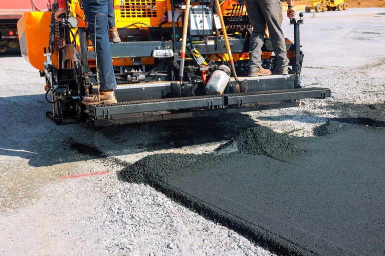Construction workers operating paving machine to lay new asphalt on road construction site